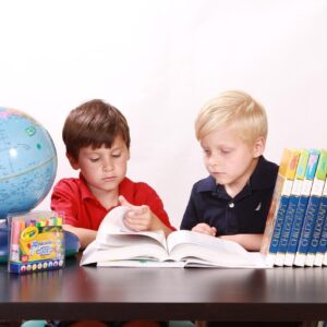 two kids learning together at a table with books and a globe