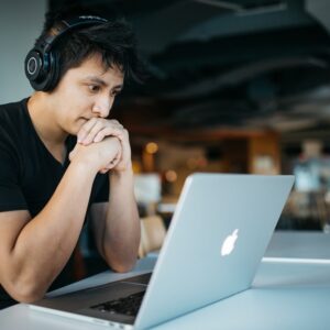 A young man wearing headphones works on his laptop studying AP math.