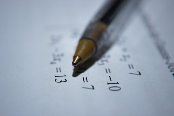 A close-up of a pen resting on a sheet with algebra equations, representing ACT math topics.