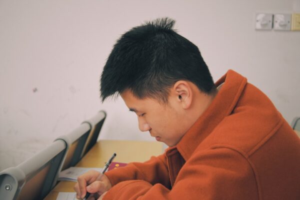 A student in an orange coat writes on a piece of paper. Many students find the PSAT is easier than the SAT.