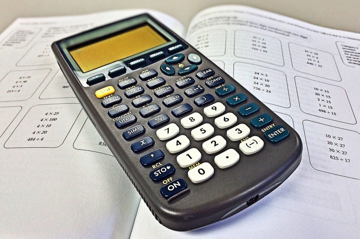 A scientific calculator resting on a math workbook with multiplication problems for 7th grade math help.