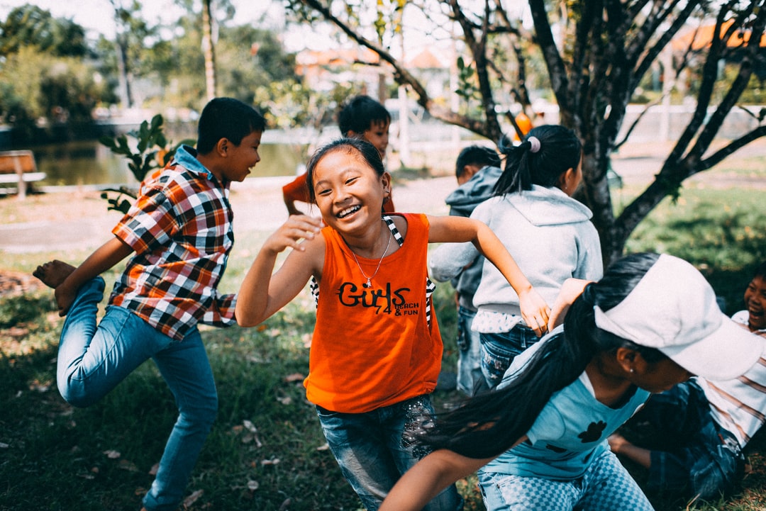 A group of four boys and three girls are smiling and playing outside