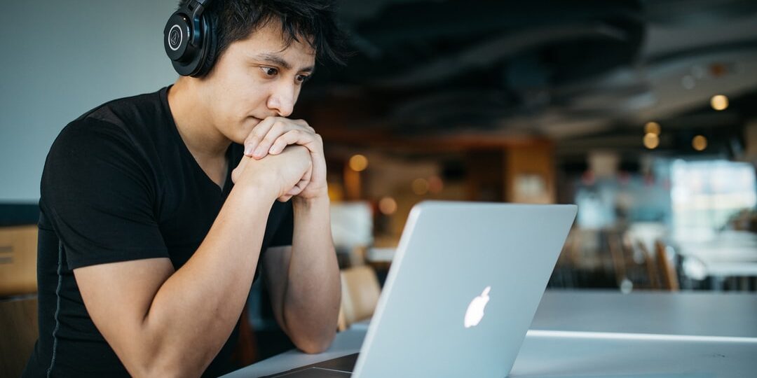 A young man wearing headphones works on his laptop studying AP math.
