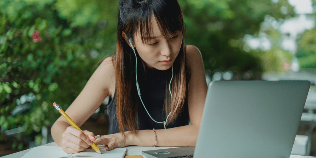 Girl with earphones, pencil in hand, and looking at a laptop